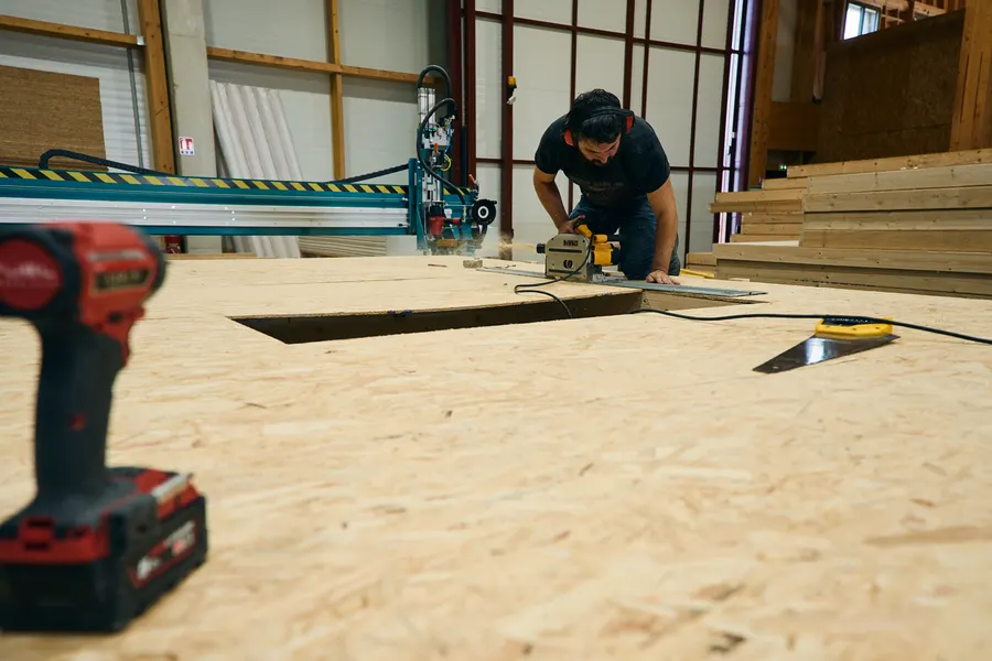Menuisier découpant un panneau de plancher à la scie circulaire, sur le chantier