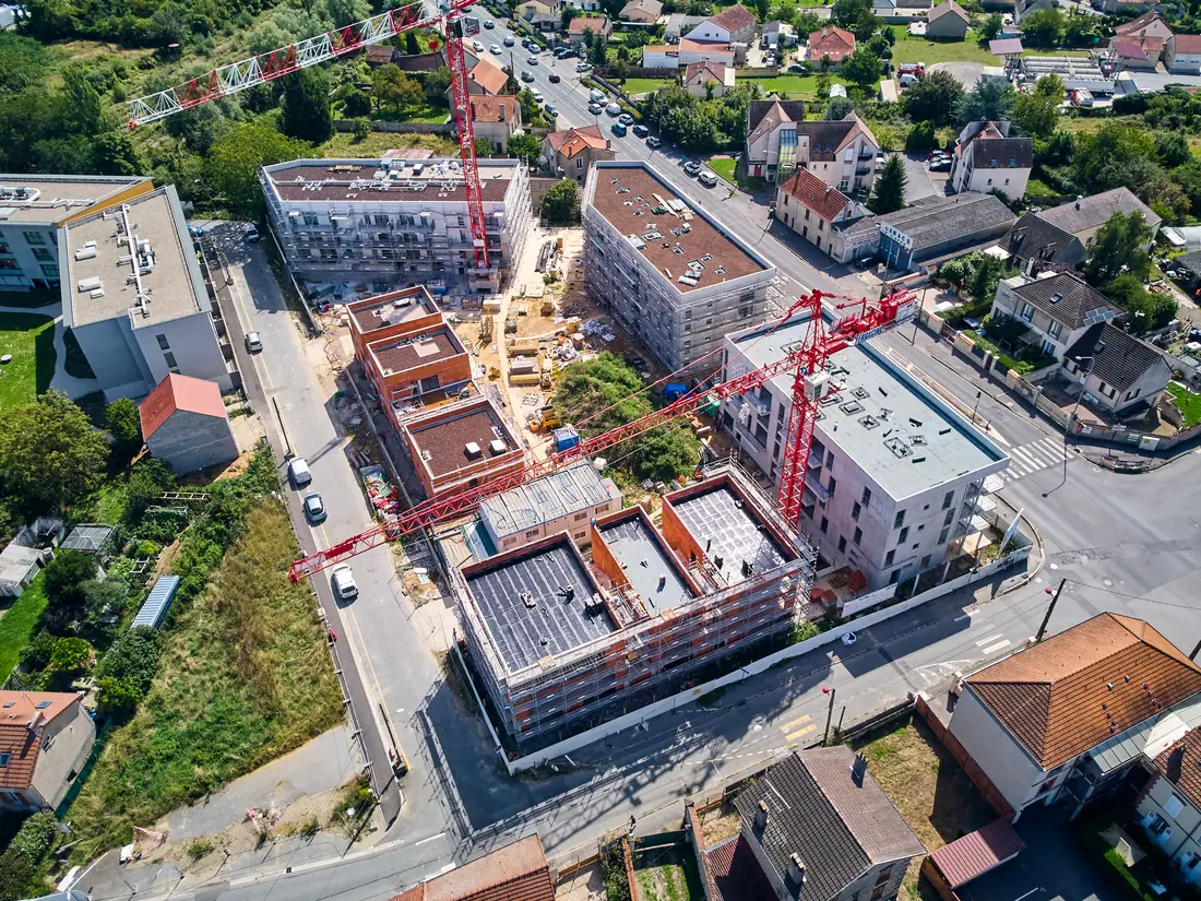 Vue aérienne d'un éco-quartier en construction : quatre immeubles et deux grues rouges