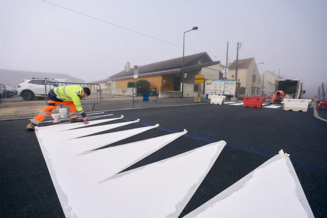 Agent de marquage traçant des chevrons blancs sur l'enrobé neuf, dans le brouillard